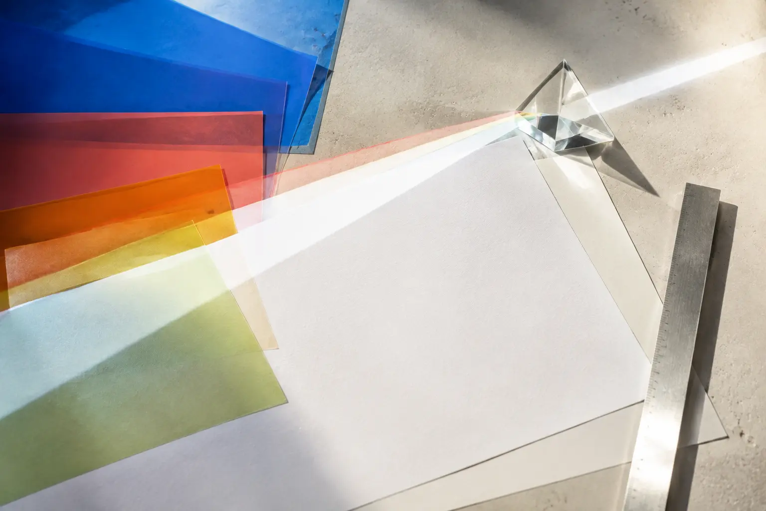Colored filters, blank editorial paper and a glass prism arranged on a drafting table